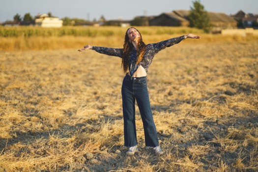 A young woman stands confidently in a vast open field, arms wide, enjoying the warmth of the sun and the beauty of nature, savoring a moment of pure freedom and joy in this serene setting