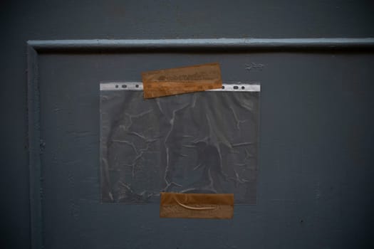 A clear plastic sheet is hanging on a grey wall with pieces of adhesive tape, creating a textured and minimalist background