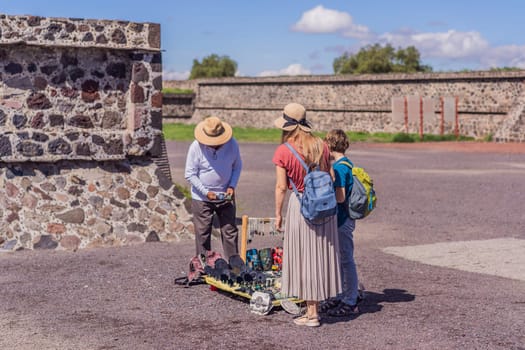 Mother and son tourists buying Mexican souvenirs from a street vendor at the foot of the Teotihuacan pyramid. Cultural experience, travel, and local craftsmanship concept.