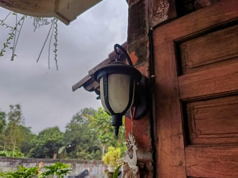Old Lamp Hanging on The Wall. It is an old lamp placed outside of a house near a wooden wall.