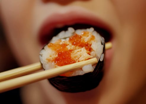 Young woman uses chopsticks to hold a sushi roll she is about to eat, Japanese food photo for menu..