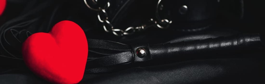 Leather whip and handcuffs for BDSM sex with red hearts as a symbol of Valentine's day holiday with love and sex with submission. Panoramic wide horizontal photo for banner head cover