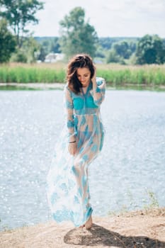 young girl with a sexy body in a swimsuit and tunic smiles on beach by lake in summer