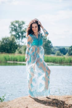 young girl with a sexy body in a swimsuit and tunic smiles on beach by lake in summer