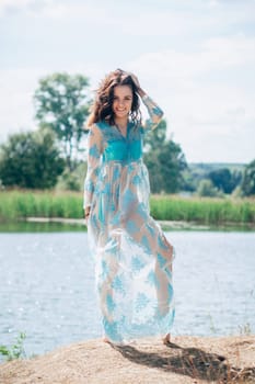 young girl with a sexy body in a swimsuit and tunic smiles on beach by lake in summer