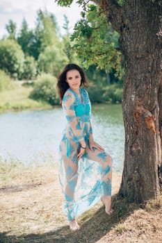 young girl with a sexy body in swimsuit and tunic poses on beach by river in summer