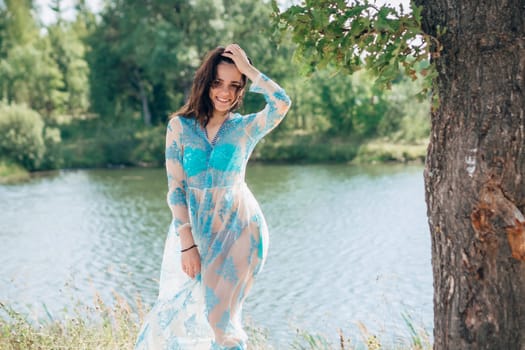 young girl with a sexy body in a swimsuit and tunic smiles on beach by lake in summer