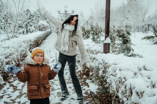Happy funny moms with a child boy son playing in the park in the snow