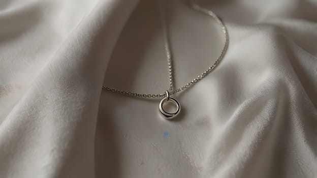 A close-up shot of a silver circle necklace on a smooth white fabric backdrop. The necklace features a simple yet elegant design with a delicate chain and a circular pendant. The soft, natural light creates a subtle sheen on the silver, highlighting its beauty. This image is perfect for showcasing jewelry designs, creating a sense of luxury, or adding a touch of elegance to your projects.,