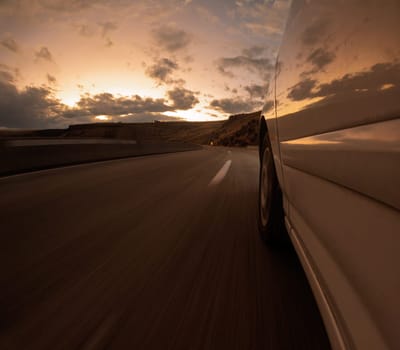 A car travels along an open road under a dramatic sunset sky, embodying freedom and adventure. The scene captures the essence of travel with a sense of motion and tranquility.