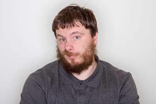 Portrait of a thoughtful, bearded man in a grey shirt. He gazes inquisitively, expressing curiosity and introspection against a neutral background. Suitable for themes of contemplation