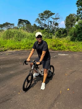Healthy lifestyle, bicycle sport and exercise, a man in casual sportswear rides a bicycle on a sunny day surrounded by lush greenery, the image captures a sense of relaxation and outdoor adventure, good for health and sport article or content creation