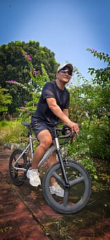 Healthy lifestyle, bicycle sport and exercise, a man in casual sportswear rides a bicycle on a sunny day surrounded by lush greenery, the image captures a sense of relaxation and outdoor adventure, good for health and sport article or content creation