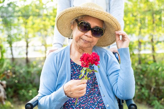 Asian senior woman holding red rose flower, smile and happy in the sunny garden.