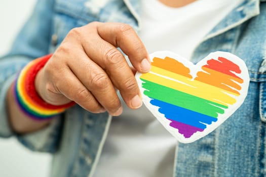 Asian lady wearing rainbow flag wristbands and hold red heart, symbol of LGBT pride month celebrate annual in June social of gay, lesbian, bisexual, transgender, human rights.