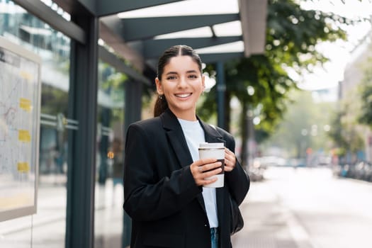 Beautiful young multiracial hispanic business woman using public transportation in city smiling and holding eco thermo cup with coffee.