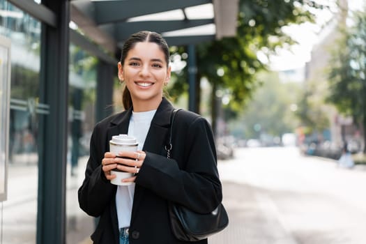 Beautiful young multiracial hispanic business woman using public transportation in city smiling and holding eco thermo cup with coffee.