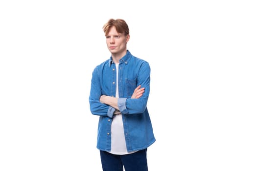 young handsome man with red hair in a blue shirt over a white t-shirt in a studio background.