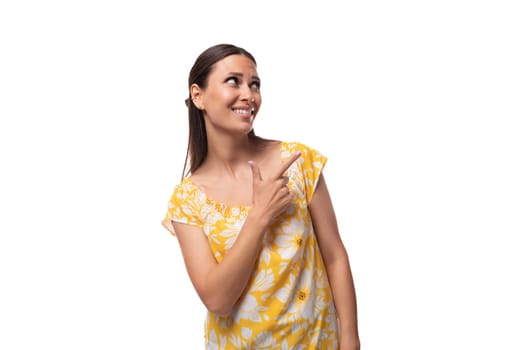 Caucasian young woman with straight black hair dressed in a yellow sundress gesturing with her fingers.