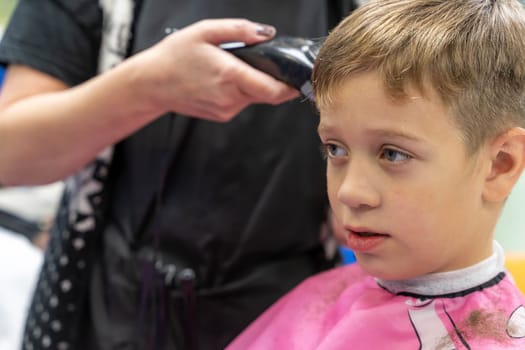 Hair cutting for a child using a hair clipper in a beauty salon. a school-age boy gets a haircut at a barber shop. a Caucasian boy in a beauty salon makes a stylish hairstyle