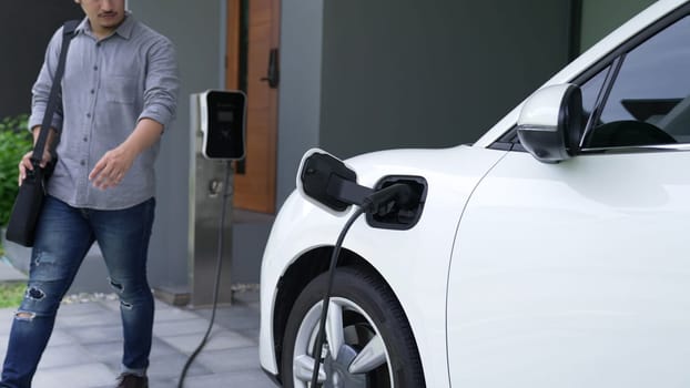 A man unplugs the electric vehicle's charger at his residence. Concept of the use of electric vehicles in a progressive lifestyle contributes to a clean and healthy environment.