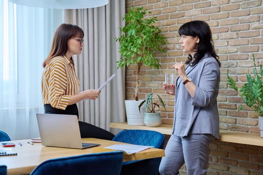 Two mature business women colleagues working together in office. Serious confident females talking, discussing business projects. 40s 50s business people, work, teamwork, communication