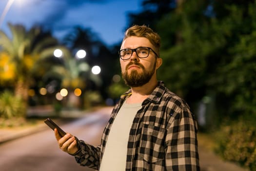 Man waits taxi by using transportation app on night street. Technologies and city