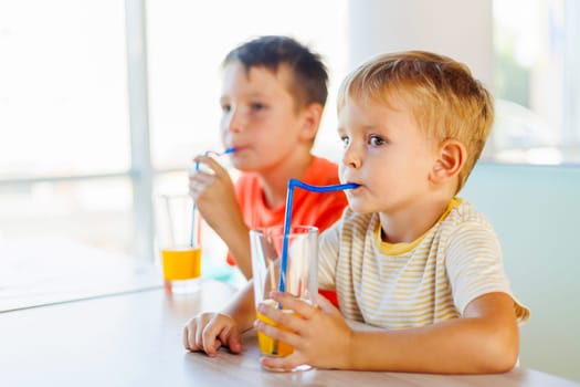 Cute children drinking soda or soft drink with straw in a fast food restaurant.