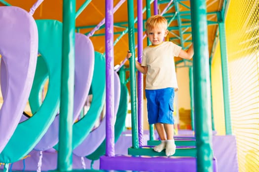 Cute little boy crawling and playing on colorful playground at indoor amusement park