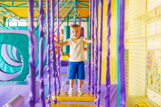 Cute little boy crawling and playing on colorful playground at indoor amusement park