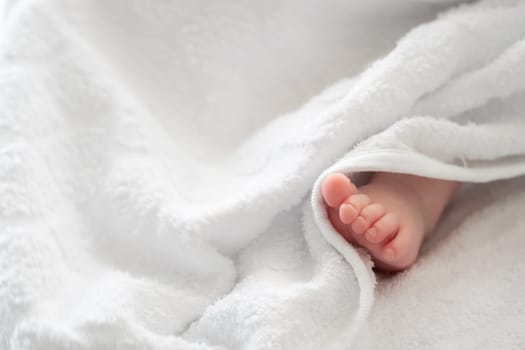 An endearing image showcasing the tiny foot of a baby, gracefully peeking out from the white embrace of a soft towel