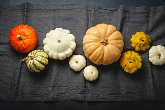 Thanksgiving festive table composition with different pumpkins on gray tablecloth runner, rustic dark table top view..