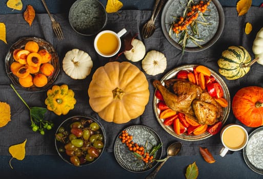 Thanksgiving festive table composition with roasted turkey, pumpkins, vegetable salad, fruit, orange beverage. Thanksgiving celebration dinner with traditional autumn meals on rustic dark table.