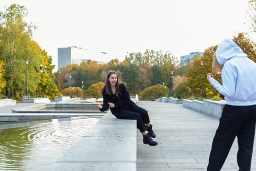 A beautiful girl playfully splashes water on her friend in an autumn park