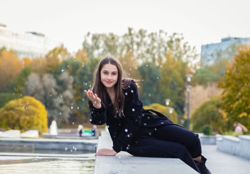 A beautiful girl playfully splashes water on her friend in an autumn park