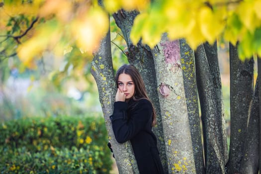 A beautiful girl stands by a tree in an autumn park