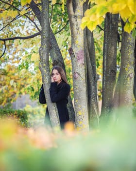 A beautiful girl stands by a tree in an autumn park