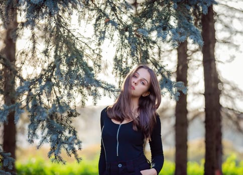 A girl stands near a blue spruce in an autumn park