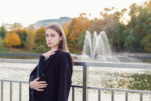 Portrait of a girl on a bridge near a pond in a city park against the backdrop of fountains