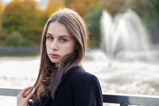 Portrait of a girl on a bridge near a pond in a city park against the backdrop of fountains