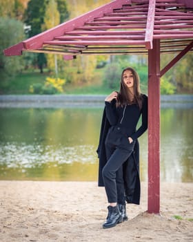 A beautiful girl poses while standing by a pond under an umbrella in an autumn park