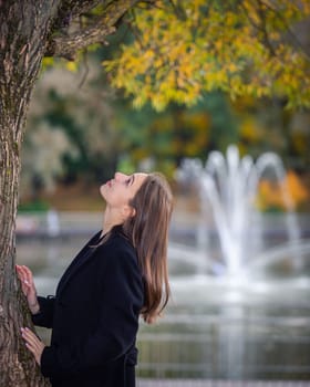 Portrait of a girl near a tree in a city park against the backdrop of fountains
