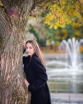 Portrait of a girl near a tree in a city park against the backdrop of fountains