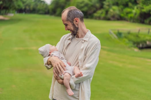 A happy 40-year-old father cradles her newborn in a sun-drenched park. Love, family and generations in harmony.