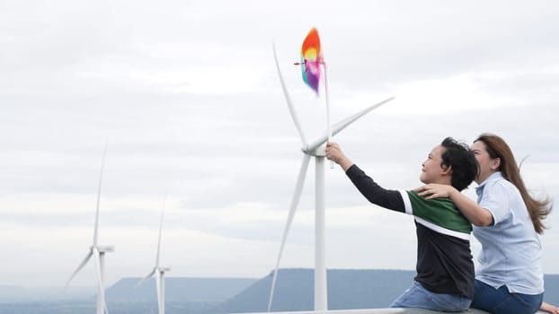 Progressive happy mother and her son at the wind turbine farm. Electric generator from wind by wind turbine generator on the country side with hill and mountain on the horizon.