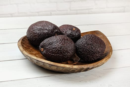 Dark brown ripe avocados ( bilse variety)  in wooden carved bowl on white boards desk