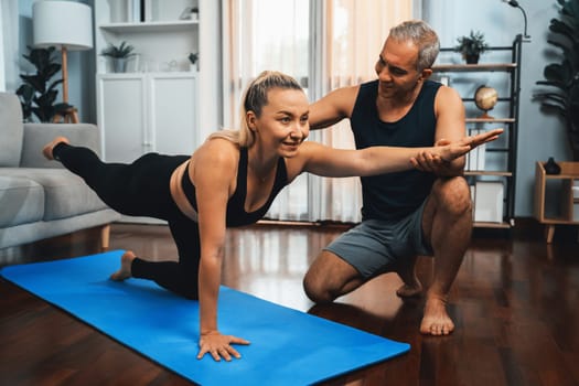 Happy active senior couple in sportswear being supportive and assist on yoga posture together at home. Healthy senior man and woman lifestyle with yoga exercise. Clout