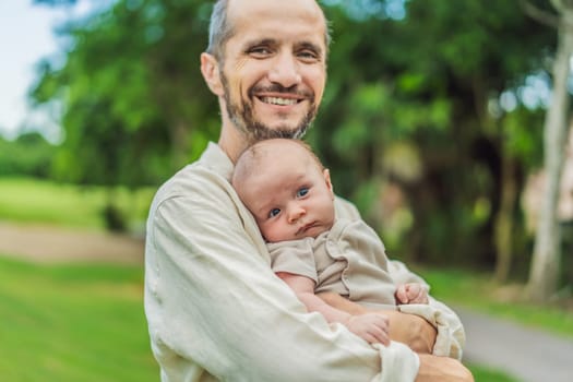 A happy 40-year-old father cradles her newborn in a sun-drenched park. Love, family and generations in harmony.