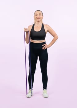 Full body length shot athletic and sporty senior woman with fitness resistance band on isolated background. Healthy active physique and body care lifestyle after retirement. Clout