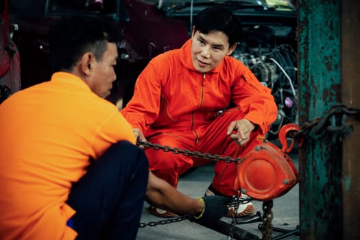 Mechanic testing strength and reliability of chain hoist for car towing in car workshop garage. Automotive service worker ensure through inspection of mechanical equipment. Oxus